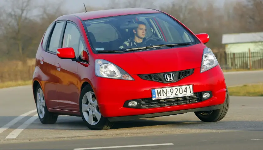 Czerwony Honda Jazz z młodym kierowcą za kierownicą. Wiele osób szuka honda jazz opinie przed zakupem.