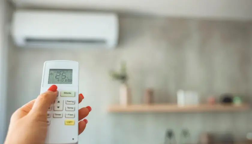 Mano con control remoto para cambiar temperatura aire acondicionado. Pantalla muestra 25°C.