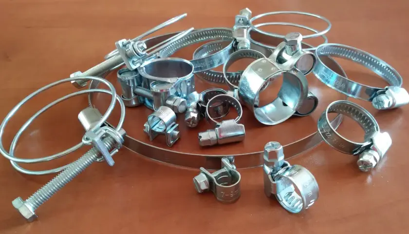 Metalowe opaski zaciskowe, czyli trytytki, w różnych rozmiarach, leżą na drewnianym blacie.