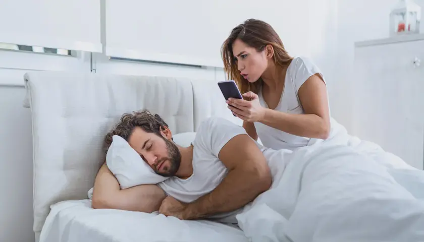 Donna preoccupata controlla il telefono del partner addormentato, un classico esempio di psicologia della sfiducia.