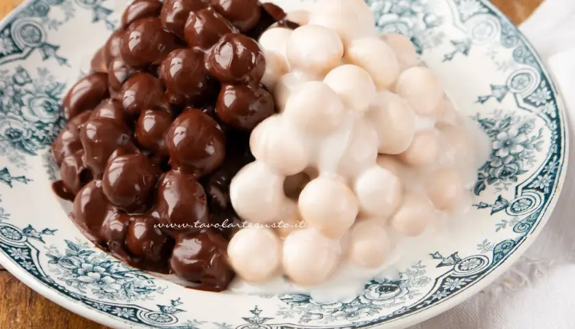 Pignolata messinese: palline dolci ricoperte di cioccolato fondente e glassa bianca, servite su un piatto decorato.