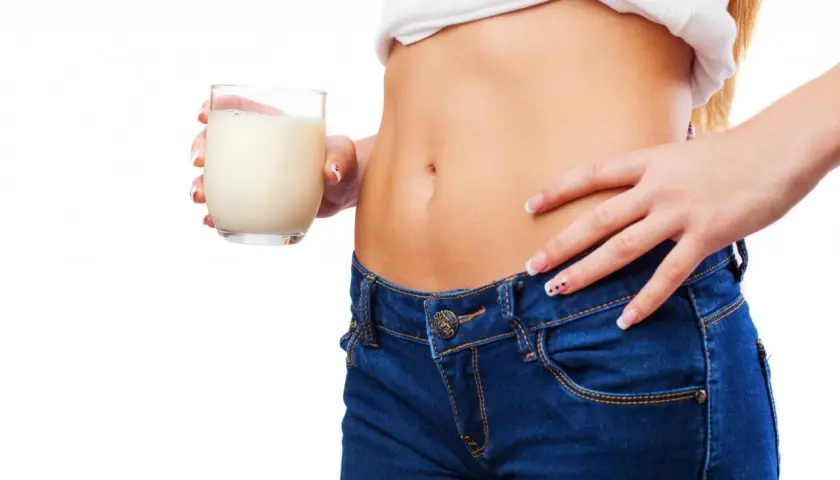 Donna con jeans e maglietta bianca tiene un bicchiere di latte. Un aiuto per capire cosa bere per andare in bagno velocemente.