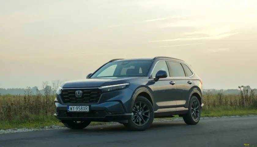 Ciemnoniebieski Honda CR-V Hybrid na tle zachodzącego słońca, zaparkowany na poboczu drogi.