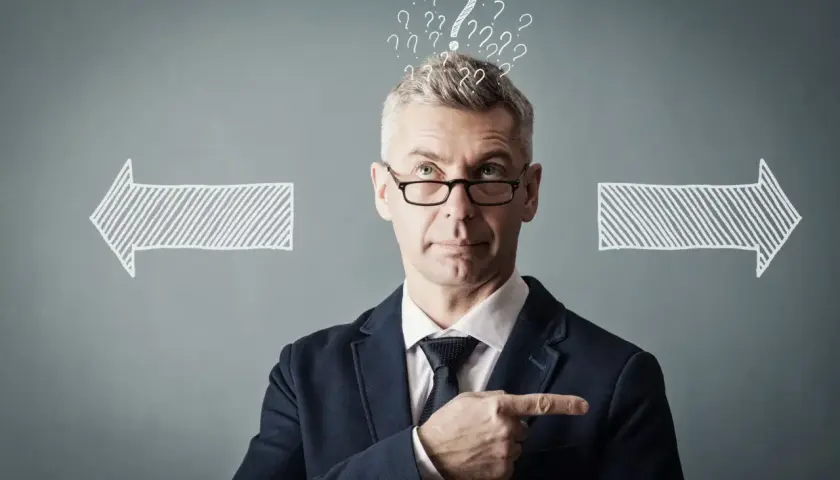 Un homme d'affaires réfléchit, entouré de points d'interrogation et de flèches. Il cherche la meilleure solution, peut-être avec un logiciel GED.