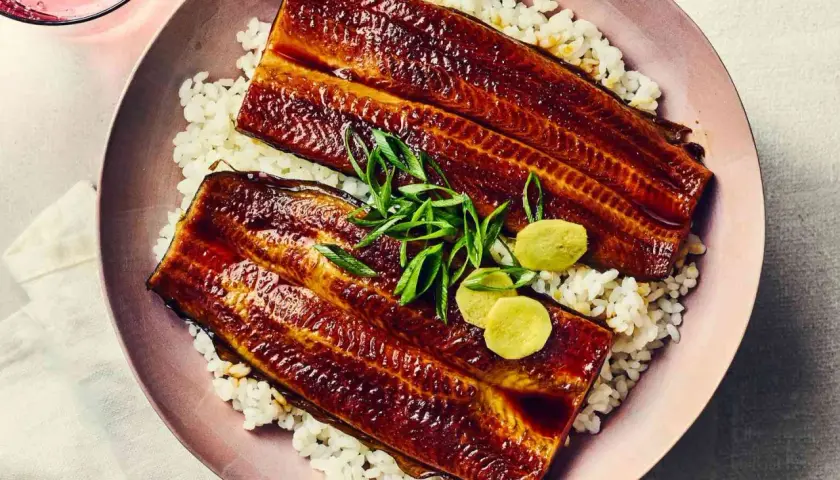 Two glazed unadon fillets rest on a bed of white rice, garnished with green onions and pickled ginger.