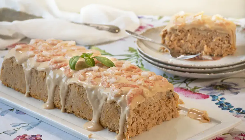 Pastel de pescado al horno cubierto con salsa cremosa y camarones. Una rebanada ya servida en un plato.