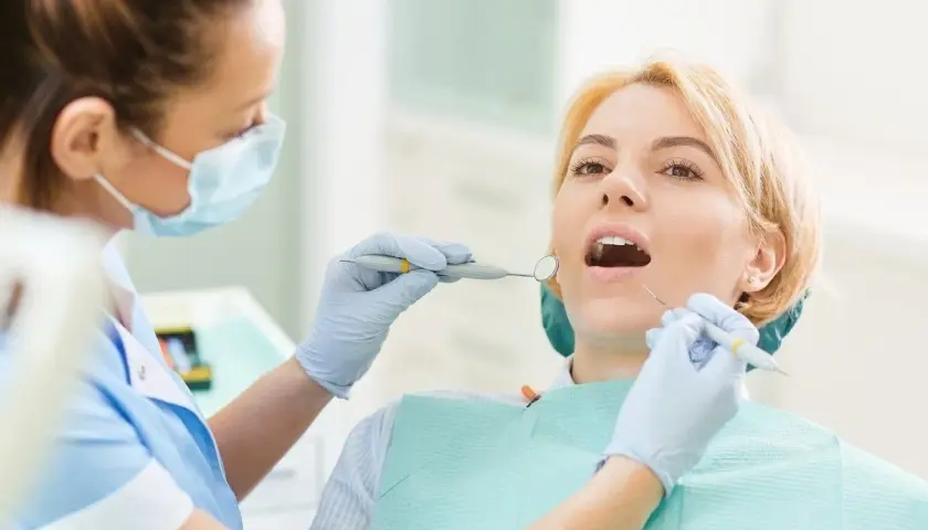 Dentystka bada zęby pacjentki narzędziami stomatologicznymi.