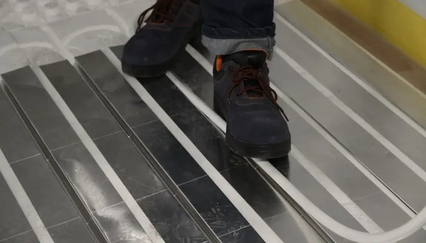 Praca nad tym, jak zrobić ogrzewanie podłogowe w starym domu, postępuje. Widać buty robocze na aluminiowych płytach systemu.