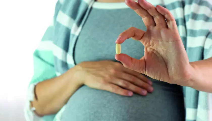 Mujer embarazada muestra una pastilla, una solución para saber como quitar acidez estomago.