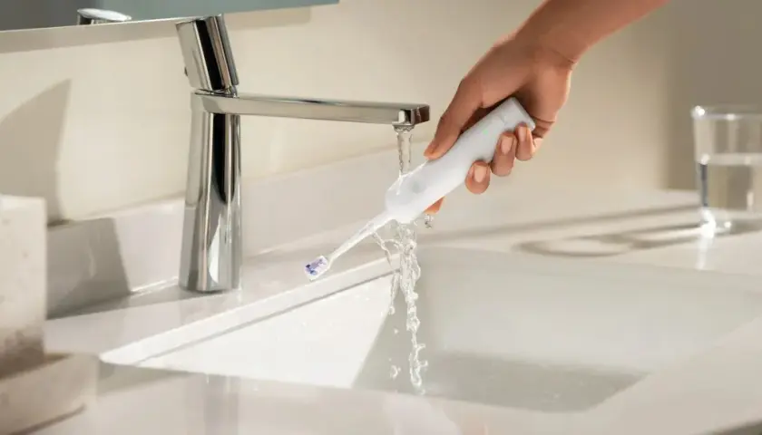 Mano che sciacqua uno spazzolino elettrico sotto un rubinetto. Ideale per chi soffre di gengive ritirate.