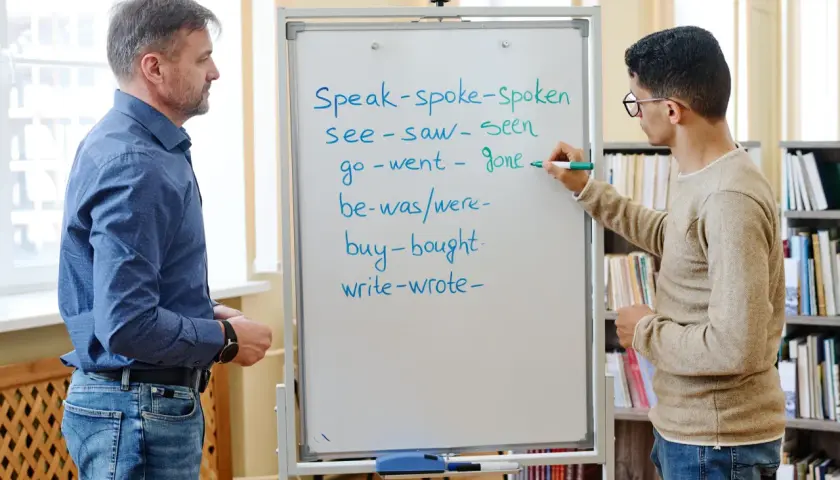 Un insegnante e uno studente studiano il passato in inglese. Lo studente scrive verbi irregolari sulla lavagna.