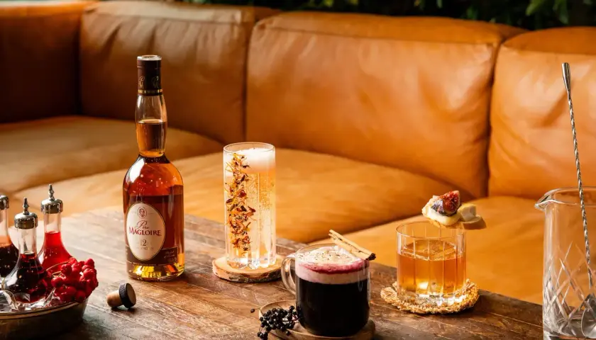 En flaska Calvados står bredvid drinkar och tillbehör på ett träbord.