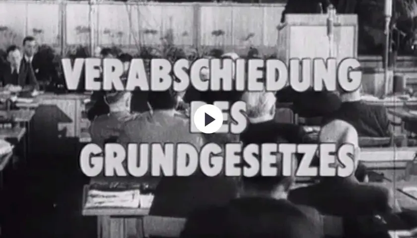 Der parlamentarische Rat verabschiedet das Grundgesetz. Männer in Anzügen sitzen und stehen im Saal.