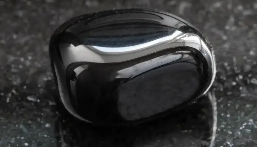 Glatter, glänzender onyx stein liegt auf einer dunklen, gesprenkelten Oberfläche.