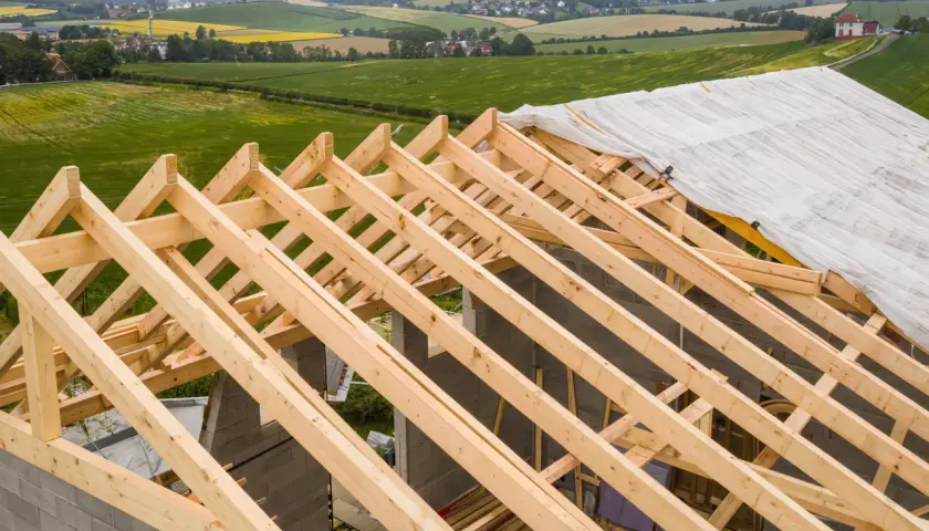 Charpente en bois sur un chantier, recouverte d'une bâche. La question est : combien de temps peut-on laisser une charpente dehors avant qu'elle ne se dégrade ?