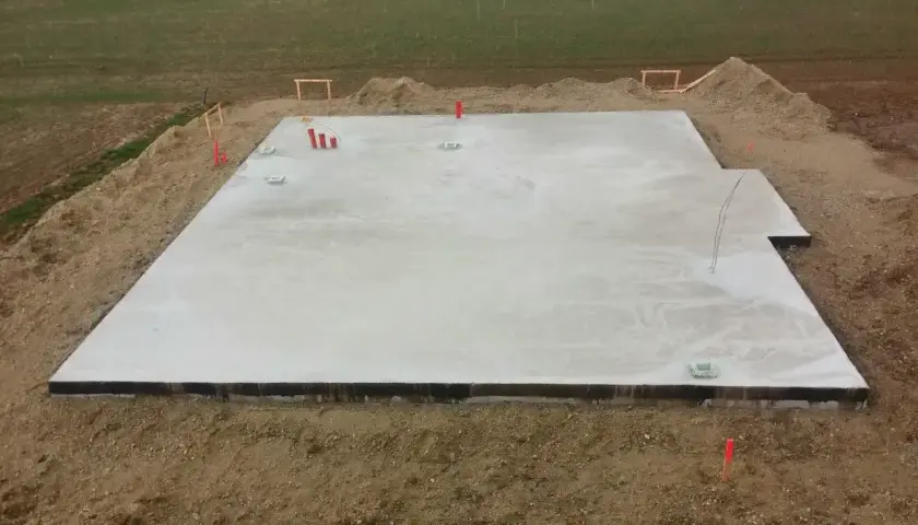Nowa płyta fundamentowa gotowa na budowę domu. Widać wystające rury i elementy instalacji.