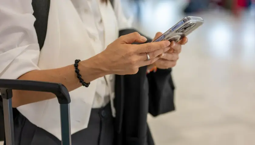 Kobieta z telefonem w dłoni, obok walizki. Sprawdza informacje o wyłączeniu 3G Plus, przygotowując się do podróży.
