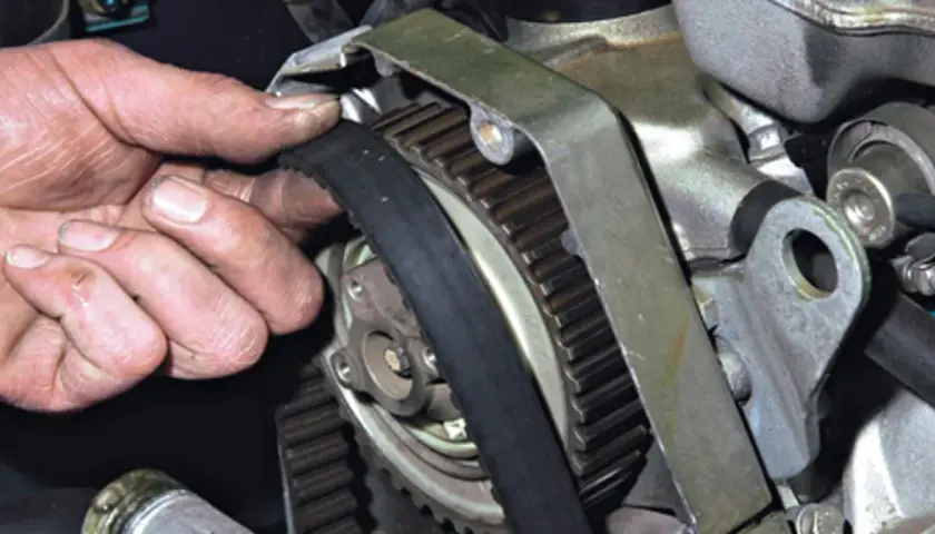 Dłoń mechanika sprawdza stan paska rozrządu, kluczowego elementu silnika.