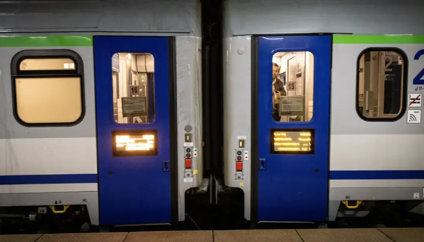 Dwa wagony kolejowe z niebieskimi drzwiami i oknami. Widać numery wagonów 16 i 15. Różne rodzaje wagonów czekają na pasażerów.