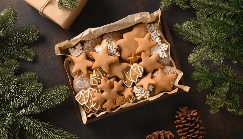 Kiste mit selbstgemachten Weihnachtsplätzchen, Sternen und Bäumen, perfekt zum Basteln von Weihnachtsgeschenken. Tannenzweige und Zapfen schmücken die Szene.