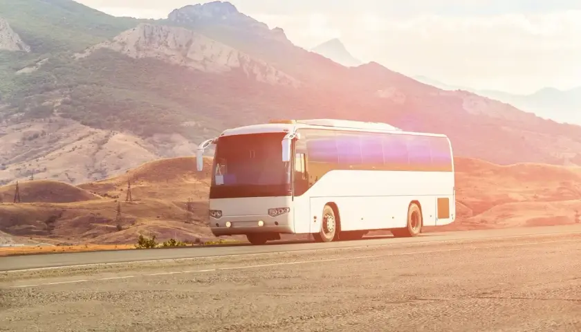 Biały autokar jedzie drogą w malowniczym, górzystym krajobrazie. Kierowca autobusu wiezie pasażerów w podróż.