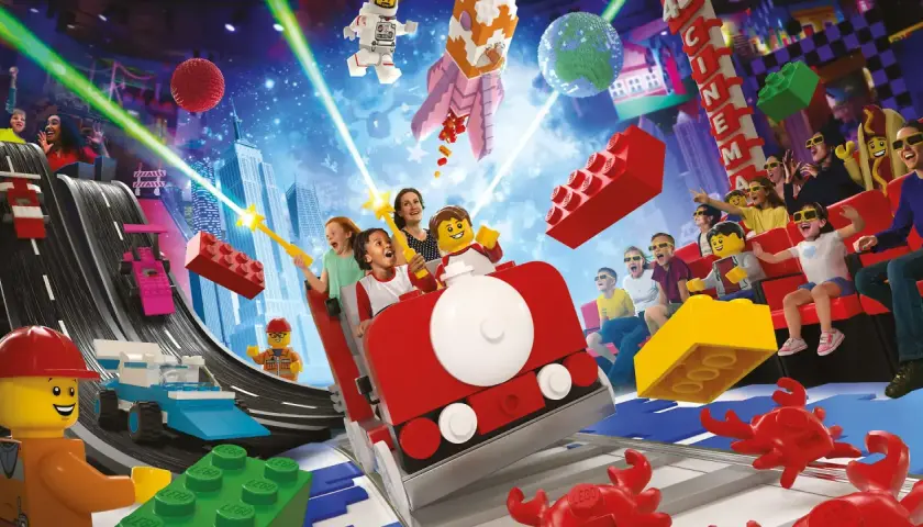 Lego Masters erleben eine Achterbahnfahrt voller Action und Spaß, mit Raketen, Rennwagen und einem Kino im Hintergrund.