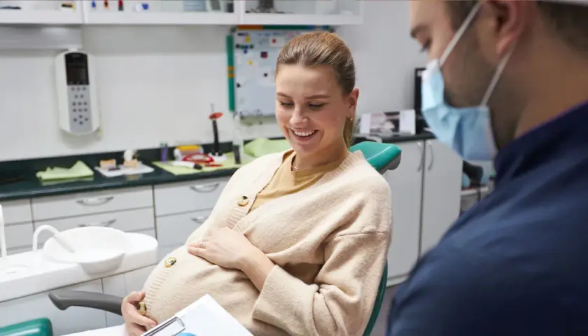 Donna incinta sorride dal dentista, preoccupata per la carie in gravidanza.