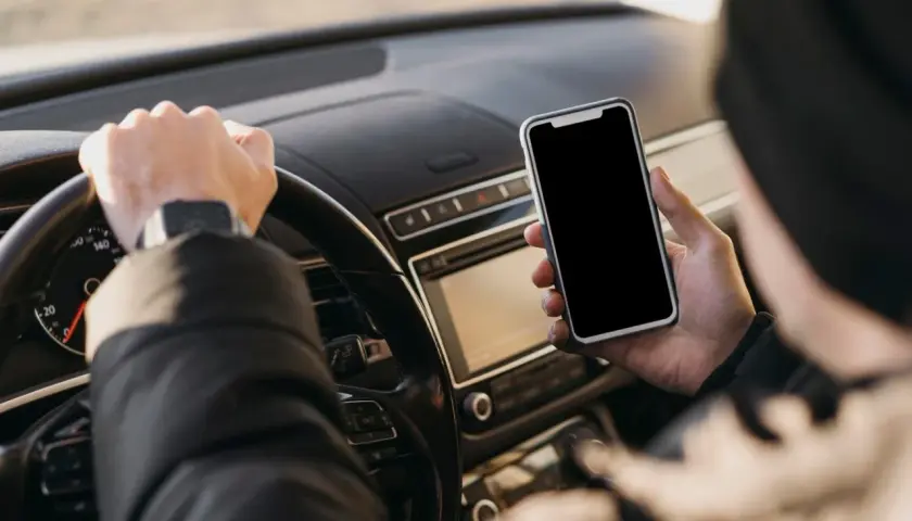 Kierowca trzyma telefon podczas jazdy, ryzykując mandat za telefon.