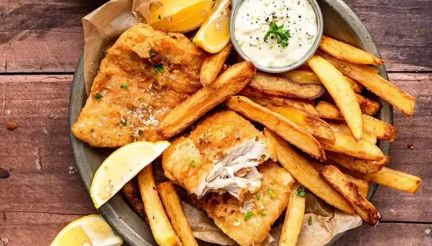 Chrupiące **fish and chips** z cytryną i sosem tatarskim na drewnianym stole. Idealna przekąska!