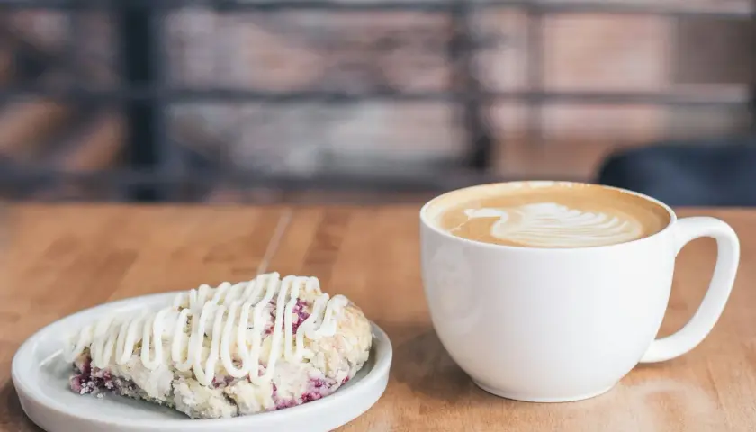 Ein Latte Macchiato mit schönem Milchschaum-Muster und ein Scone mit Zuckerguss. Perfekt für den Nachmittagstee, fast so gut wie selbst gemacht, wie man einen Latte Macchiato macht.