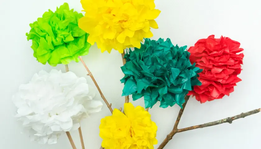 Bunte Seidenblumen basteln: Fünf Papierblumen in Rot, Grün, Gelb und Weiß auf Holzästen vor weißem Hintergrund.