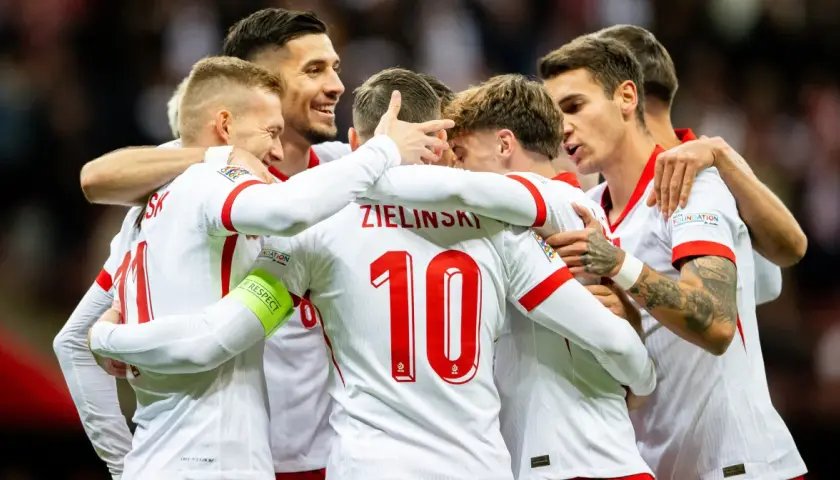 Piłkarze reprezentacji Polski w białych strojach świętują razem, przytulając się.