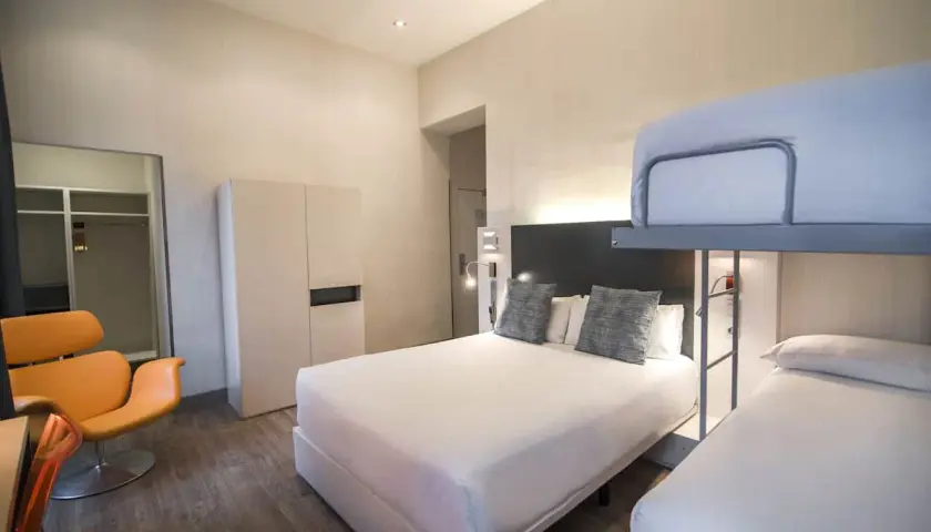 Habitación familiar en Petit Palace Canalejas Sevilla con cama doble, litera y sillón naranja.