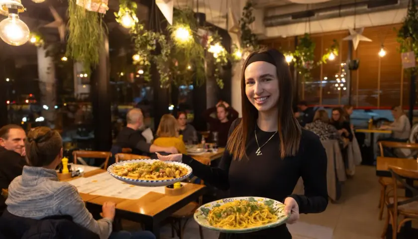 Uśmiechnięta kelnerka serwuje pyszne dania w najlepszej włoskiej restauracji we Wrocławiu. Aromatyczne makarony kuszą z talerzy.