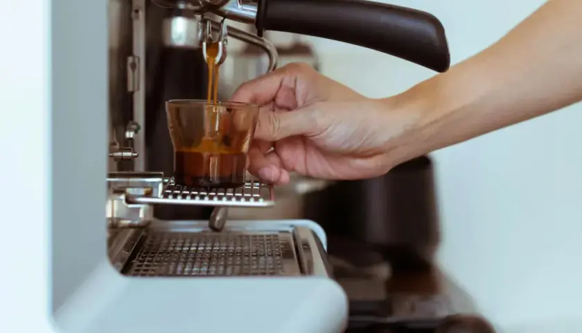 Eine Hand hält ein Glas, während frisch gebrühter Espresso manuell zubereitet wird.