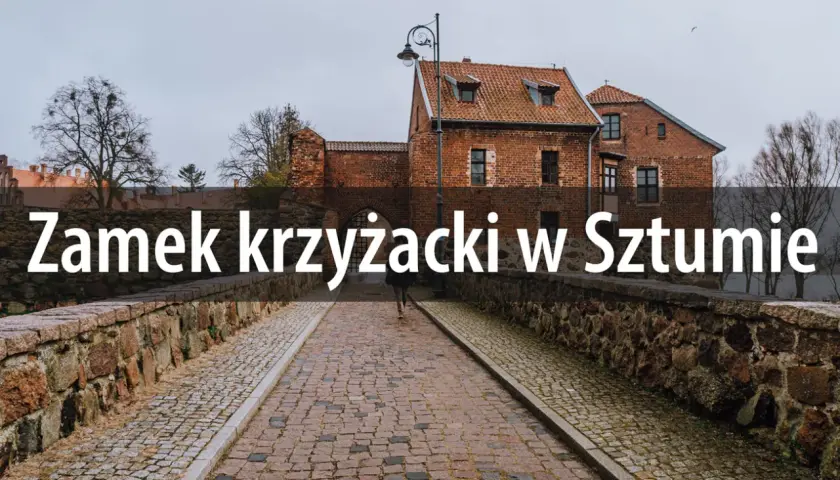 Kamienny most prowadzi do ceglanego zamku krzyżackiego w Sztumie. W oddali widać drzewa i pochmurne niebo.