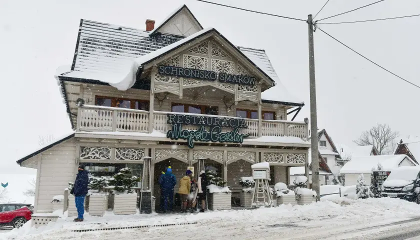 Drewniana restauracja "Schronisko Smaków" w Bukowinie Tatrzańskiej, pokryta śniegiem, z neonem "Restauracja".