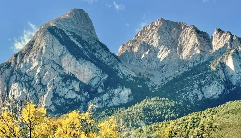 Majestuosas montañas de el Pedraforca bajo un cielo azul. El sol ilumina las cumbres rocosas y los bosques verdes.