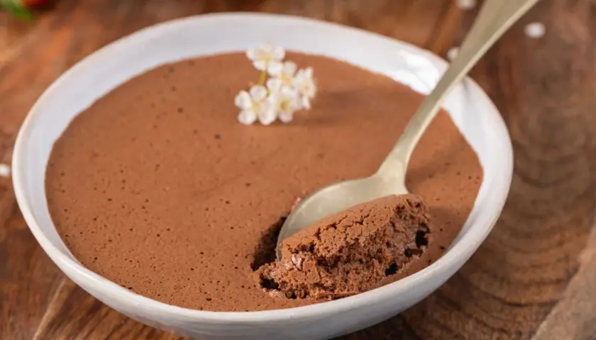 Une cuillère prend une bouchée d'une mousse au chocolat au lait aérienne, décorée de petites fleurs blanches.