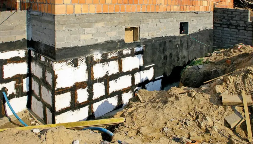 Nowe ściany w piwnicy z izolacją i siatką. Budowa fundamentów domu.