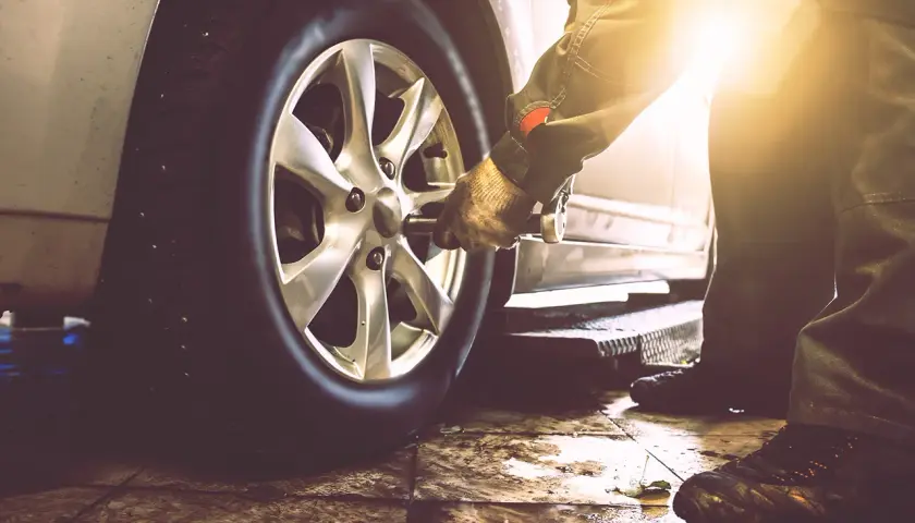 Mechanik w rękawicy używa klucza do odkręcenia koła samochodu. Pokazane jest, jak odkrecic kolo.