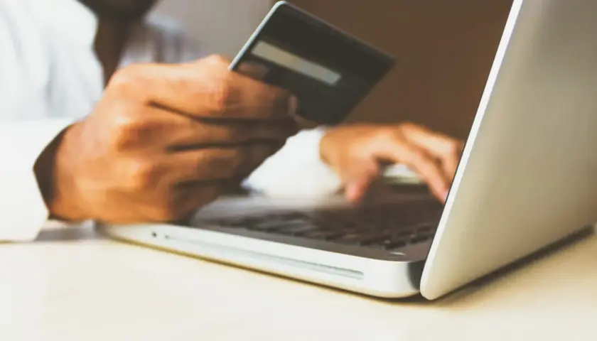 Mężczyzna z kartą kredytową w dłoni wpisuje dane na laptopie, realizując swój hedonizm w zakupach online.