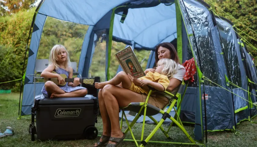 Mama czyta dzieciom w namiocie w Polsce. Jedno dziecko gra na ukulele, drugie słucha bajki. Idealne miejsce, gdzie pod namiot z dziećmi w Polsce.