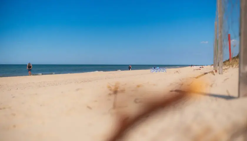 Słoneczna plaża w Niechorzu, idealne miejsce na relaks. W oddali widać ludzi spacerujących brzegiem morza.