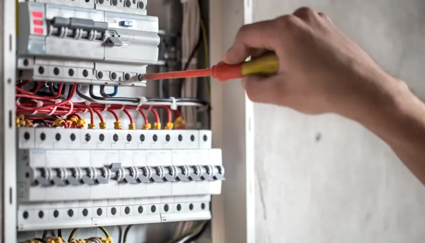 Elektryk przy skrzynce z bezpiecznikami. Dowiedz się, jak obliczyć, ile prądu zużyje urządzenie, sprawdzając jego moc.