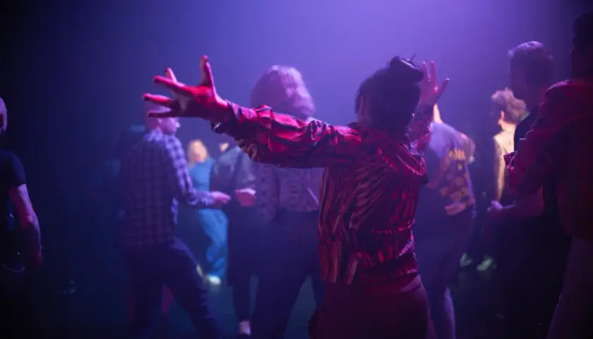 Publiken njuter av en konsert på kulturhuset. En kvinna i röd mönstrad tröja dansar med armarna uppsträckta.