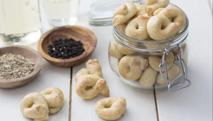 Taralli que es: crujientes bocaditos horneados, algunos en un frasco, con granos de pimienta y hinojo cerca.