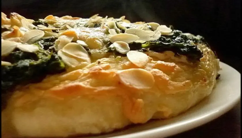 Eine köstliche Spinat Pizza mit knusprigem Teig und gerösteten Mandelblättchen. Dampf steigt auf und verspricht ein warmes, herzhaftes Gericht.