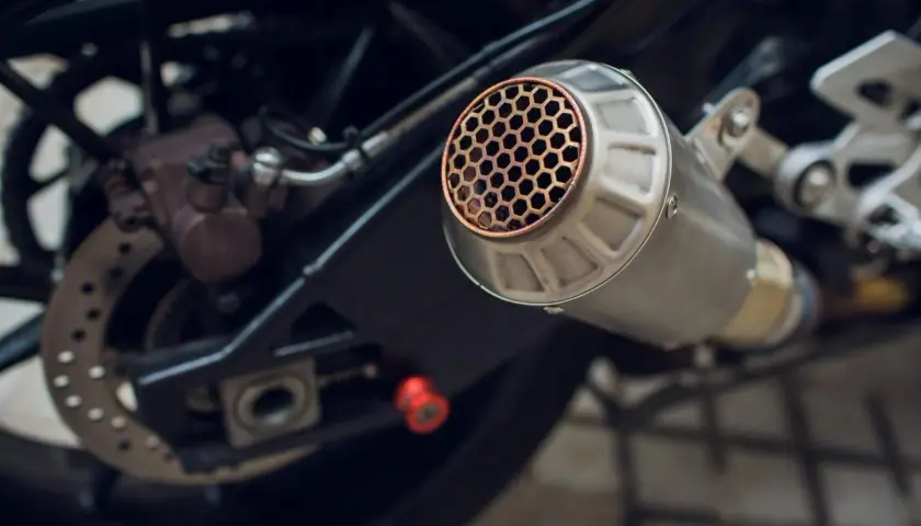 Scarico moto con griglia a nido d'ape, un **db killer fai da te** per un suono più discreto. Si intravede la ruota posteriore e il freno.