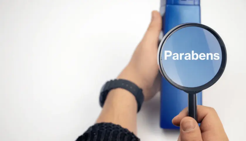 Lupa amplía la palabra "Parabens" sobre un frasco azul, indicando la búsqueda de ingredientes en productos.